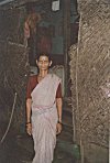 Rural woman in cotton sari in front of her thatched hut