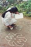 a girl looking in to a book and  drawing rangoli