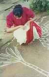 a girl looking in to a book and  drawing rangoli