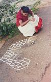 a girl looking in to a book and  drawing rangoli