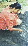 a girl looking in to a book and  drawing rangoli